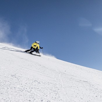 Skier in a yellow jacket skiing down a slope at Hintertux Glacier under bright sunshine.