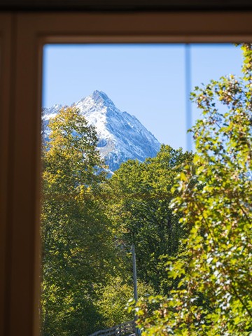 View through the window of a snow-covered mountain and green trees in Finkenberg.